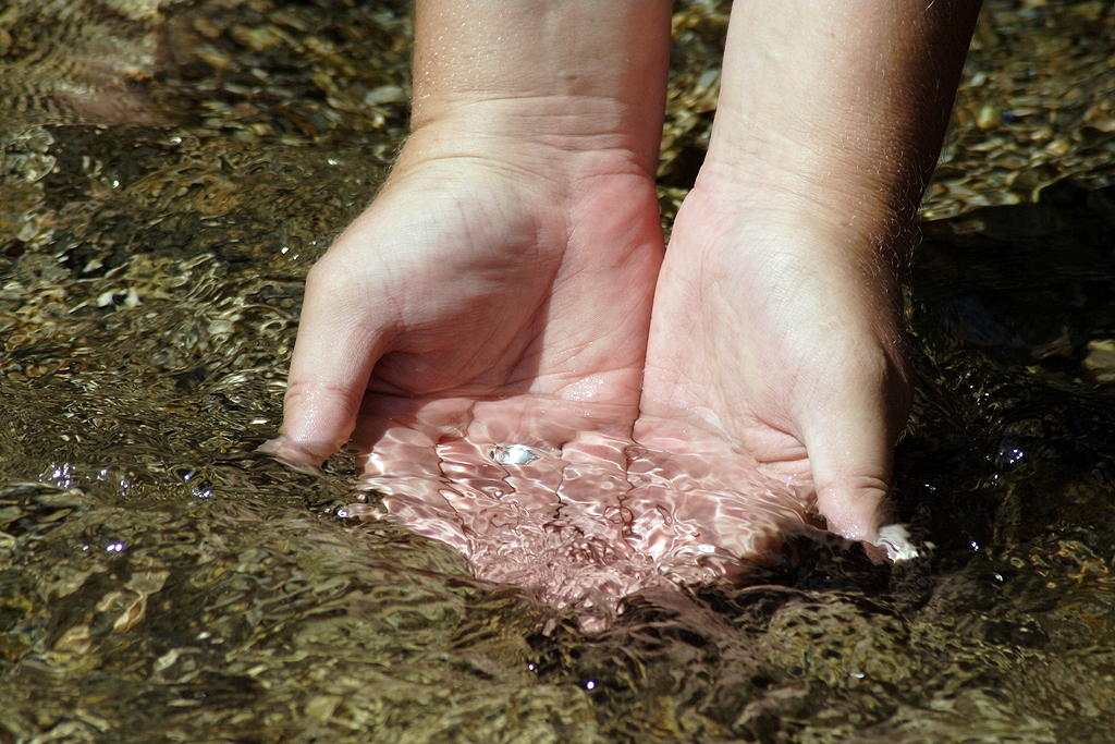 Hände schöpfen Wasser aus Bach